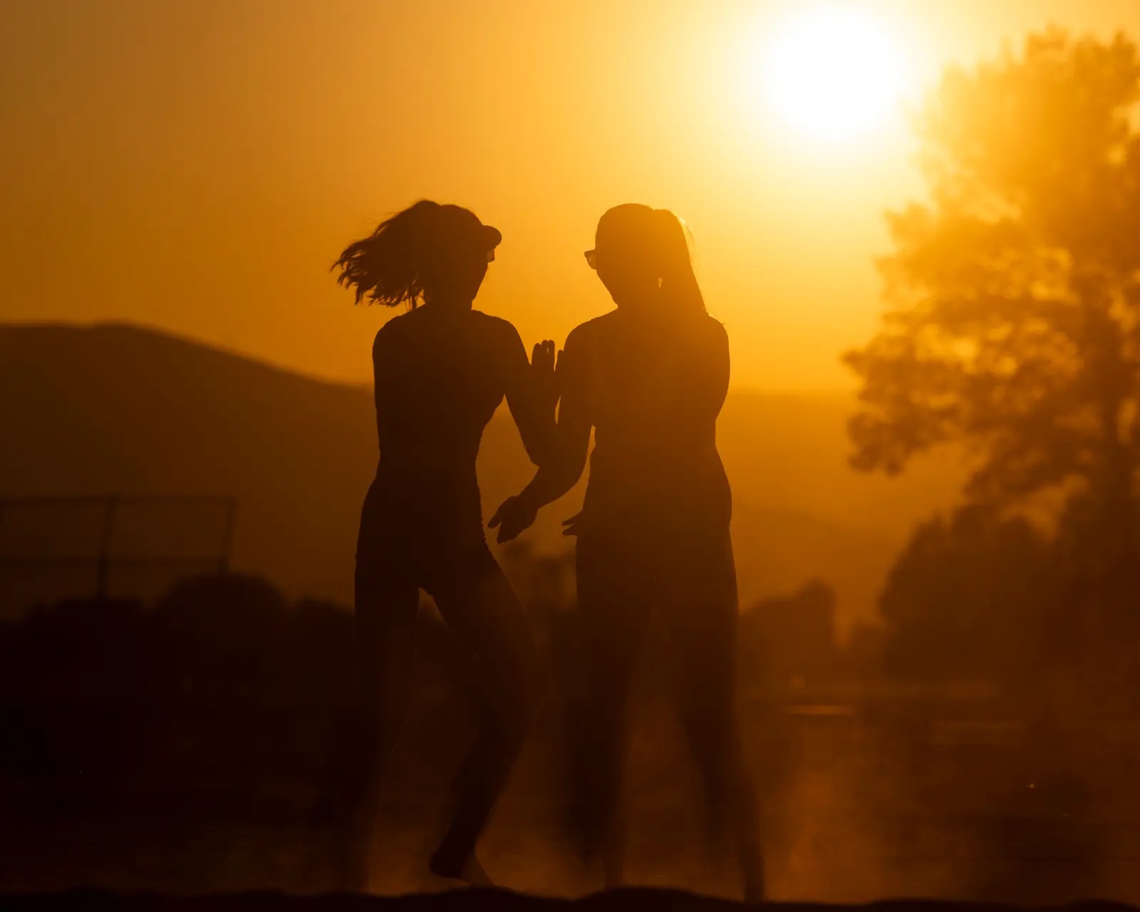 Two beach volleyball players silhouetted in warm sunset light.