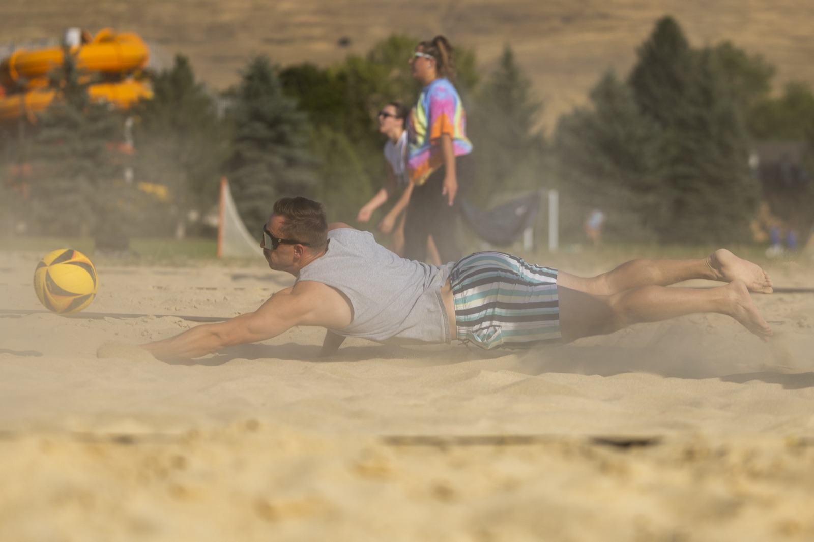 A beach volleyball player diving across the sand to reach the ball.