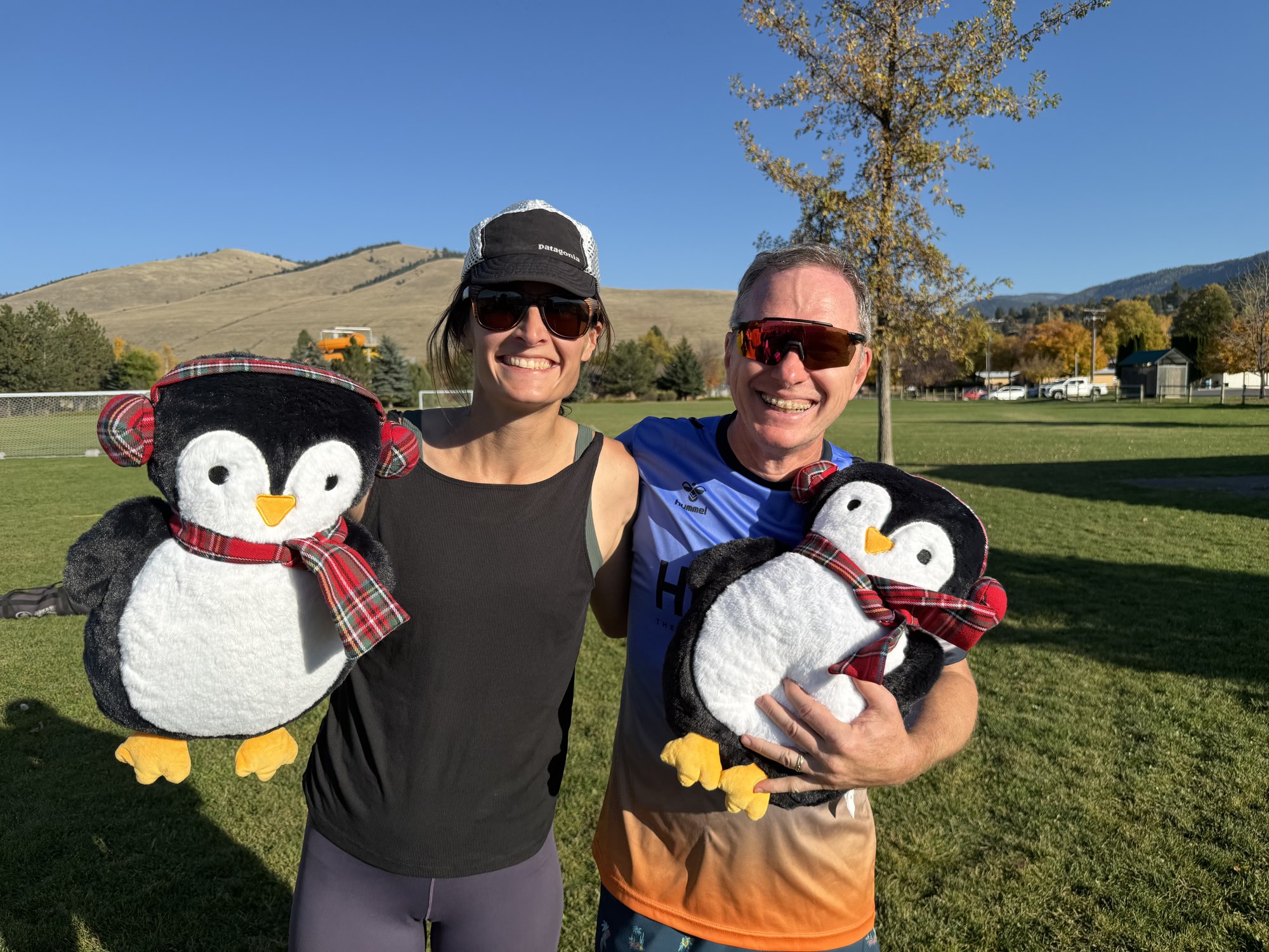 Two grass volleyball winners holding penguin prizes at FlaminGlow.